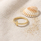 Gold Plated Cross Ring in Stainless Steel on raw linen beside a scallop shell and a scatter of fine sand