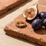 Adjustable Rainbow Gold Plated Ring on a weathered terracotta tile with a cut fig and dark plums