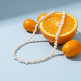 Baroque Pearl Necklace on a pale blue backdrop beside a halved orange and two kumquats