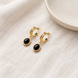 Black Onyx Drop Hoop Earrings on pale grey-green linen beside a halved lime and red currants