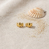 Bubble Stud Earrings on raw linen beside a scallop shell and a scatter of fine sand