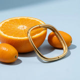 Chunky Square Bangle on a pale blue backdrop beside a halved orange and two kumquats