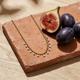Crystal Fringe Necklace on a weathered terracotta tile with a cut fig and dark plums