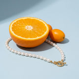Dainty Pearl Toggle Necklace on a pale blue backdrop beside a halved orange and two kumquats