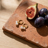 Double Pearl Hoop Earrings on a weathered terracotta tile with a cut fig and dark plums