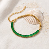 Half Emerald Half Beaded Bracelet on raw linen beside a scallop shell and a scatter of fine sand