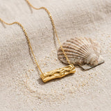 Hammered Rectangle Necklace on raw linen beside a scallop shell and a scatter of fine sand