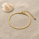 Herringbone Anklet on raw linen beside a scallop shell and a scatter of fine sand