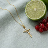 Hypoallergenic 14k Gold Plated Crucifix Pendant Necklace on pale grey-green linen beside a halved lime and red currants