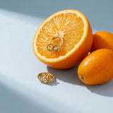 Interlocking Pave Hoops on a pale blue backdrop beside a halved orange and two kumquats