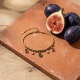 Ruby and Emerald Charm Bracelet on a weathered terracotta tile with a cut fig and dark plums