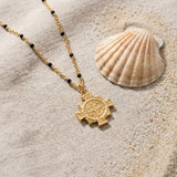 Saint Benedict Medal Necklace on raw linen beside a scallop shell and a scatter of fine sand