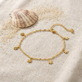 Snowflake Anklet on raw linen beside a scallop shell and a scatter of fine sand