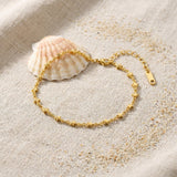 Star Chain Anklet on raw linen beside a scallop shell and a scatter of fine sand