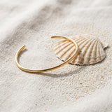 Thin Cuff Bracelet on raw linen beside a scallop shell and a scatter of fine sand