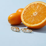 Trio Crystal Hoop Earrings on a pale blue backdrop beside a halved orange and two kumquats