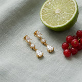 Triple CZ Drop Earrings on pale grey-green linen beside a halved lime and red currants