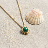 Wade Malachite Necklace on raw linen beside a scallop shell and a scatter of fine sand
