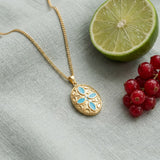 Oval Blue Petals Pendant Necklace on pale grey-green linen beside a halved lime and red currants