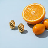 Waterproof Croissant Dome Stud Earrings on a pale blue backdrop beside a halved orange and two kumquats
