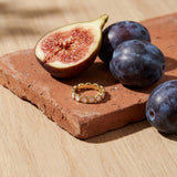 Mother of Pearl Eternity Ring on a weathered terracotta tile with a cut fig and dark plums